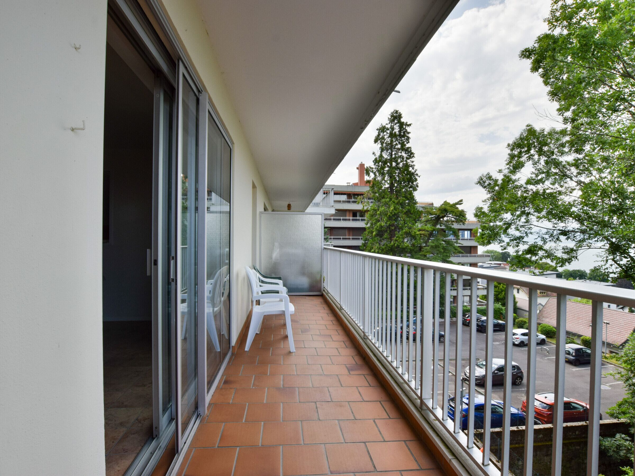 A balcony with a tiled floor, white chairs, and a railing.