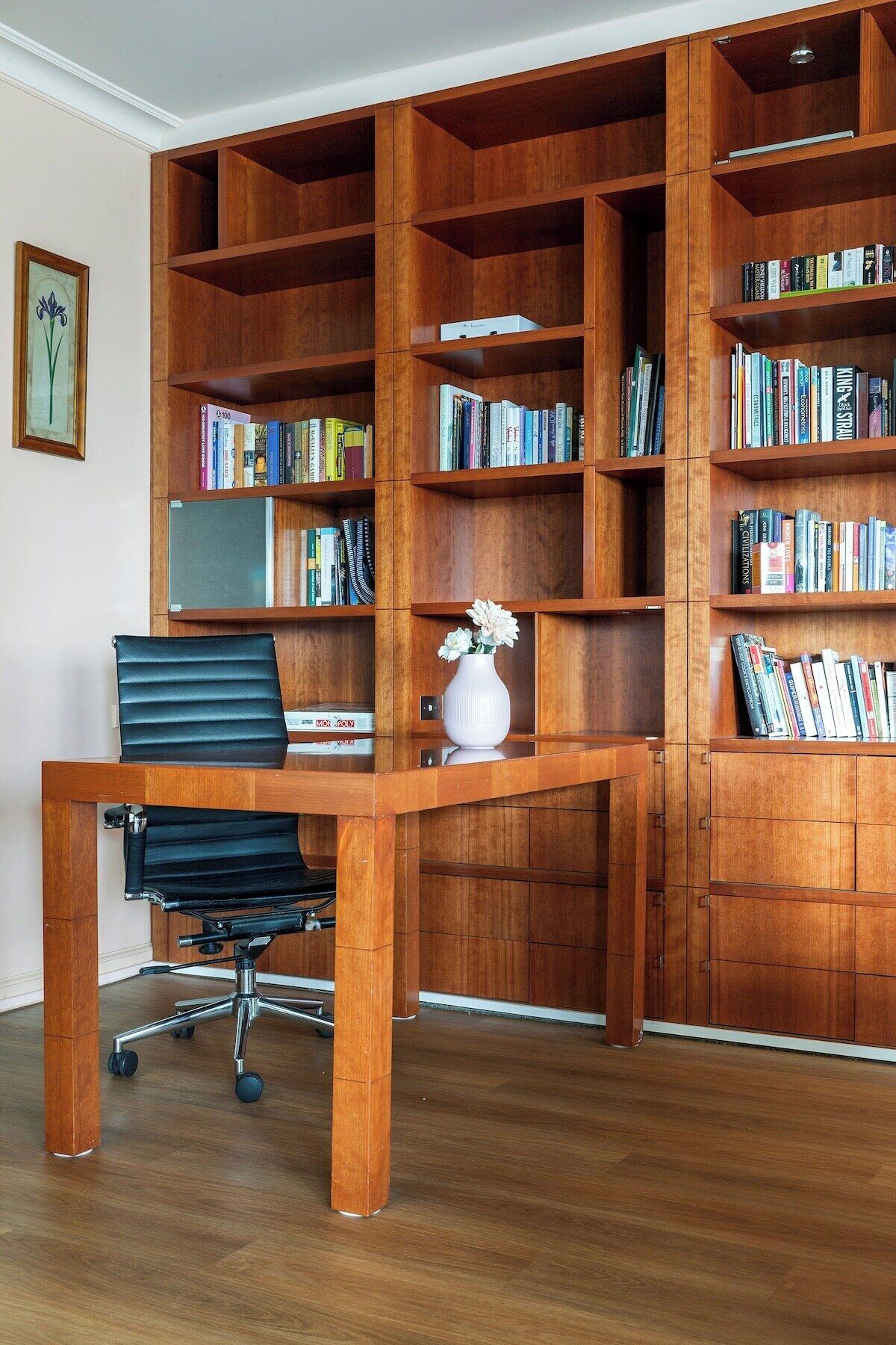 A room with a wooden desk, a black office chair, and a large bookshelf filled with books.