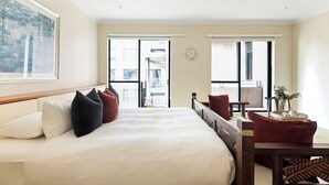 A hotel room with a large bed, a desk, and a view of the city through the windows.