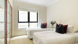Habitación de hotel con dos camas, una ventana, una mesita de noche con un florero y una puerta corredera.