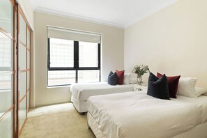Habitación de hotel con dos camas, una ventana, una mesita de noche con un florero y una puerta corredera.
