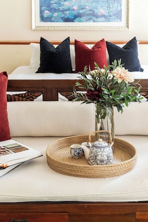 Ein ordentlich eingerichteter Raum mit einem Bett, Kissen, einer Vase mit Blumen, einer Ablage mit Teekanne und einer Zeitschrift.