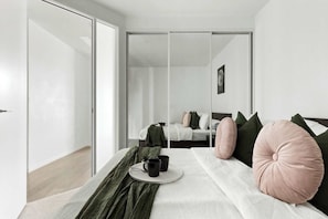 Un dormitorio moderno con una cama grande, una mesita de noche con dos tazas negras y un edredón verde.