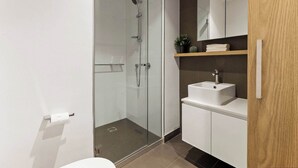 A modern bathroom with a glass-enclosed shower, a white sink, and a wooden shelf with a plant.