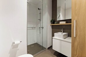 Une salle de bain moderne avec une douche à parois de verre, un lavabo blanc et une étagère en bois agrémentée d’une plante.