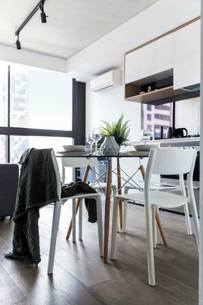 Une cuisine moderne avec des meubles blancs, une table à manger avec des chaises et une vue sur la ville grâce à de grandes fenêtres.