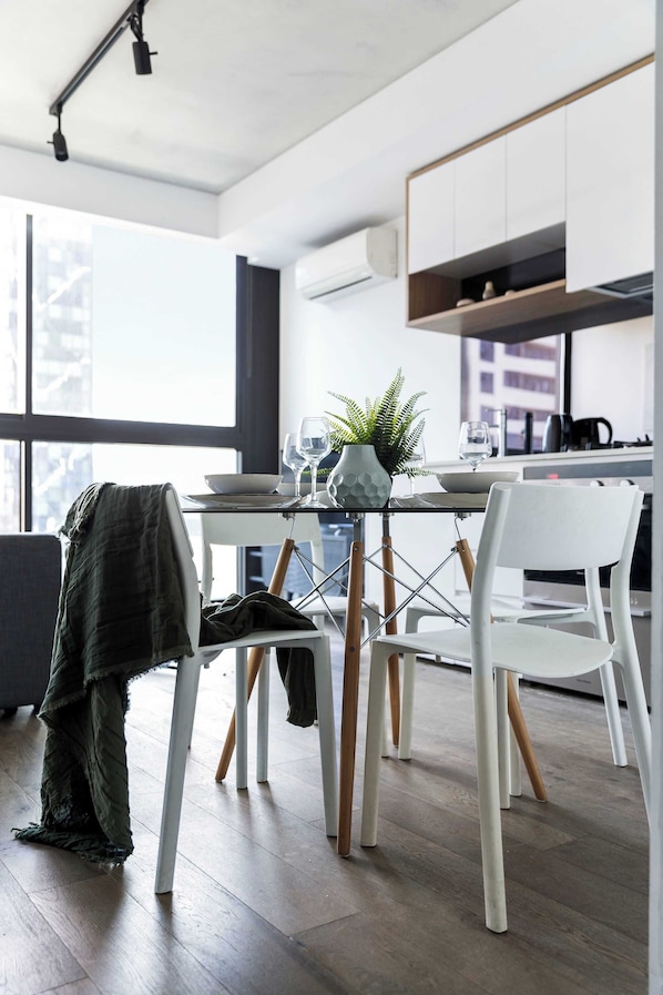 A modern kitchen with white cabinetry, a dining table with chairs, and a view of the city through large windows.