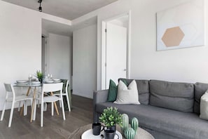 A modern living room with a grey sofa, a dining table with chairs, and a small coffee table with a plant and two black mugs.