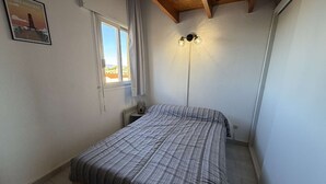Une chambre à coucher avec un lit, une fenêtre, un luminaire fixé au mur et une affiche accrochée au mur.