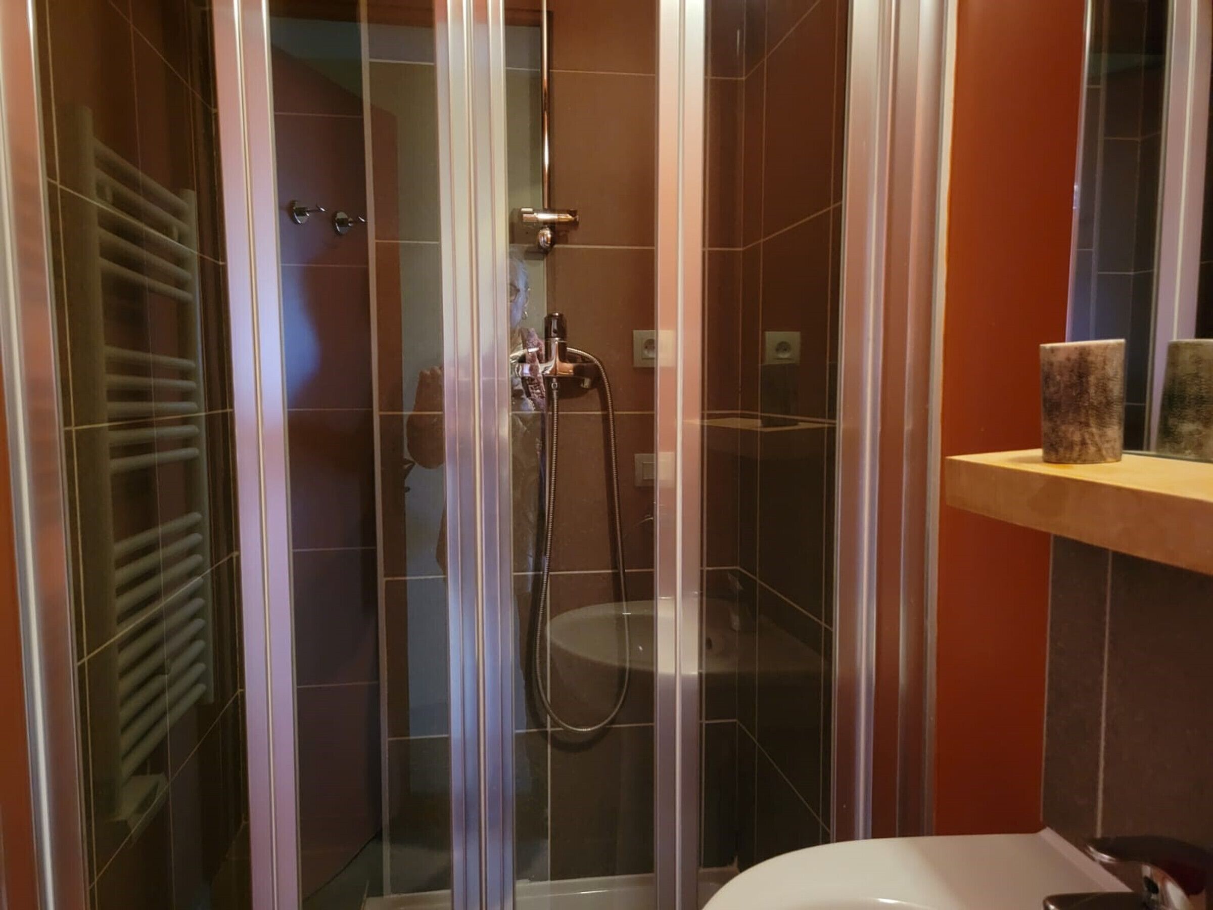 A glass-enclosed shower with a handheld showerhead and a towel rack.
