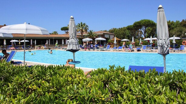 Area piscina con sedie a sdraio e ombrelloni, immersa nel verde.