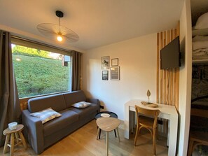 Relax in this cozy living space with a comfortable sofa, TV, and a view of the lush outdoor area.