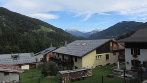 Ein Bergdorf mit traditionellen Holzhäusern, einem Steinhaufen und weiter Aussicht auf schneebedeckte Berge in der Ferne.