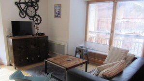 Ein Wohnzimmer mit einer Couch, einem Couchtisch, einem Fernseher auf einem Schrank und einem Fenster mit Jalousien.