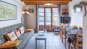 A cozy living room with a wooden ceiling, a sofa with patterned cushions, a coffee table, a TV, and a dining area with a table and chairs. - Apartment T4 for 7, parking, near ski resorts (Luz-Saint-Sauveur)