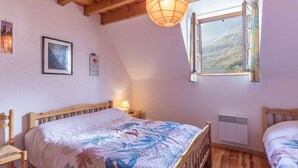 A bedroom with a wooden ceiling, a bed with a floral bedspread, a window with a view of hills, and a wall-mounted heater. - Apartment T4 for 7, parking, near ski resorts (Luz-Saint-Sauveur)