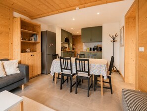 Un espacio habitable compacto con comedor, kitchenette y un sofá gris.