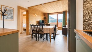 Un intérieur en bois comprenant un coin repas, une cuisine et un balcon avec vue sur la montagne.