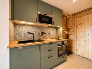 Une cuisine moderne dotée d’un four à micro-ondes encastré, d’un four en acier inoxydable et d’un plan de travail en bois.