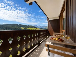 A balcony with a wooden railing, a table with food and drinks, and a scenic mountain view.
