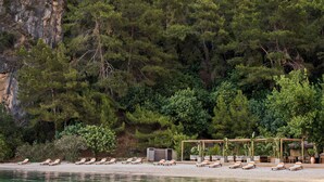 Un complexe hôtelier en bord de mer, doté de chaises longues, d’une pergola en bois et d’une structure à toit de chaume.