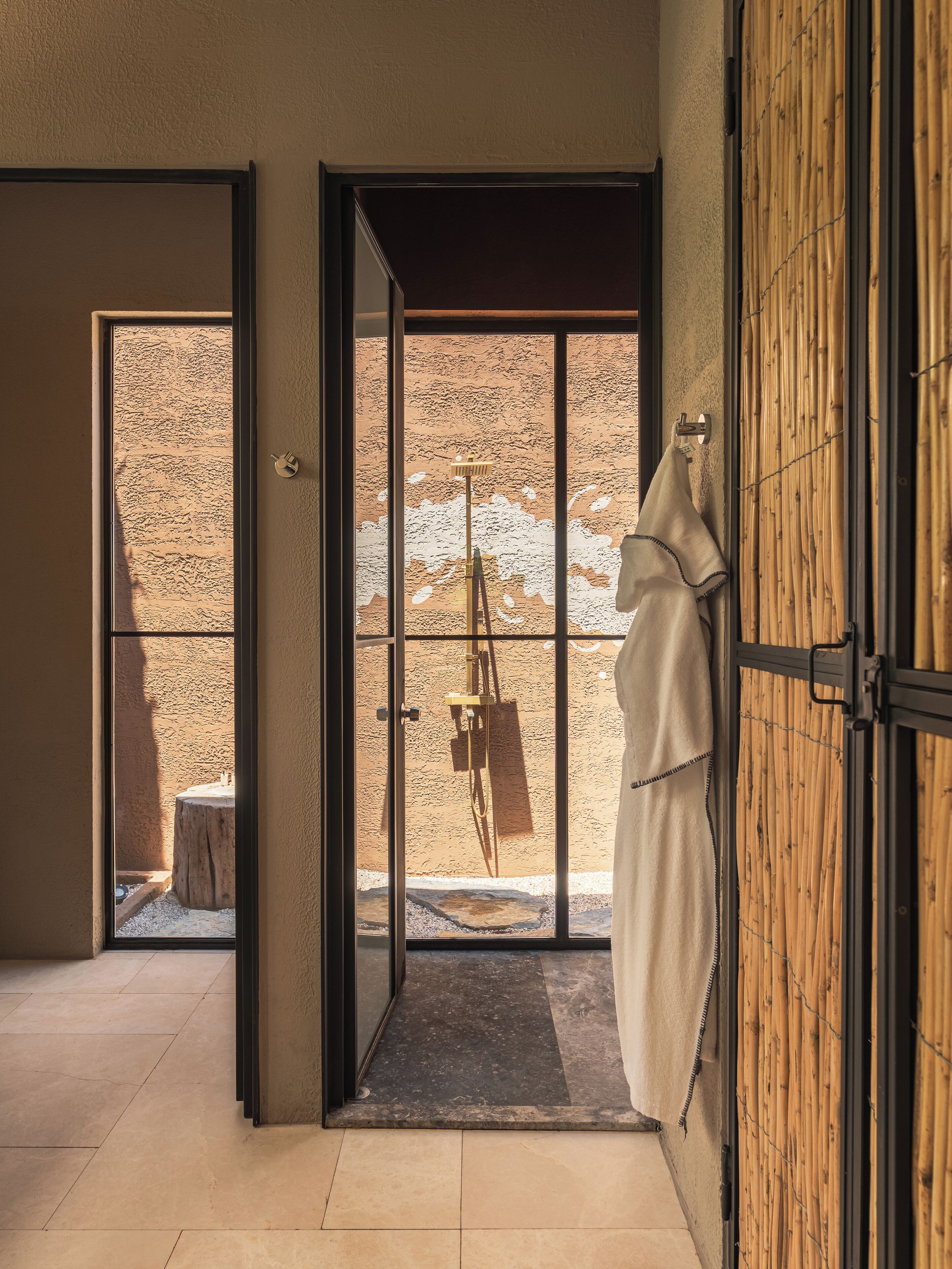 A modern bathroom with a large glass door leading to a shower area, a towel hanging on the door, and a wooden floor.