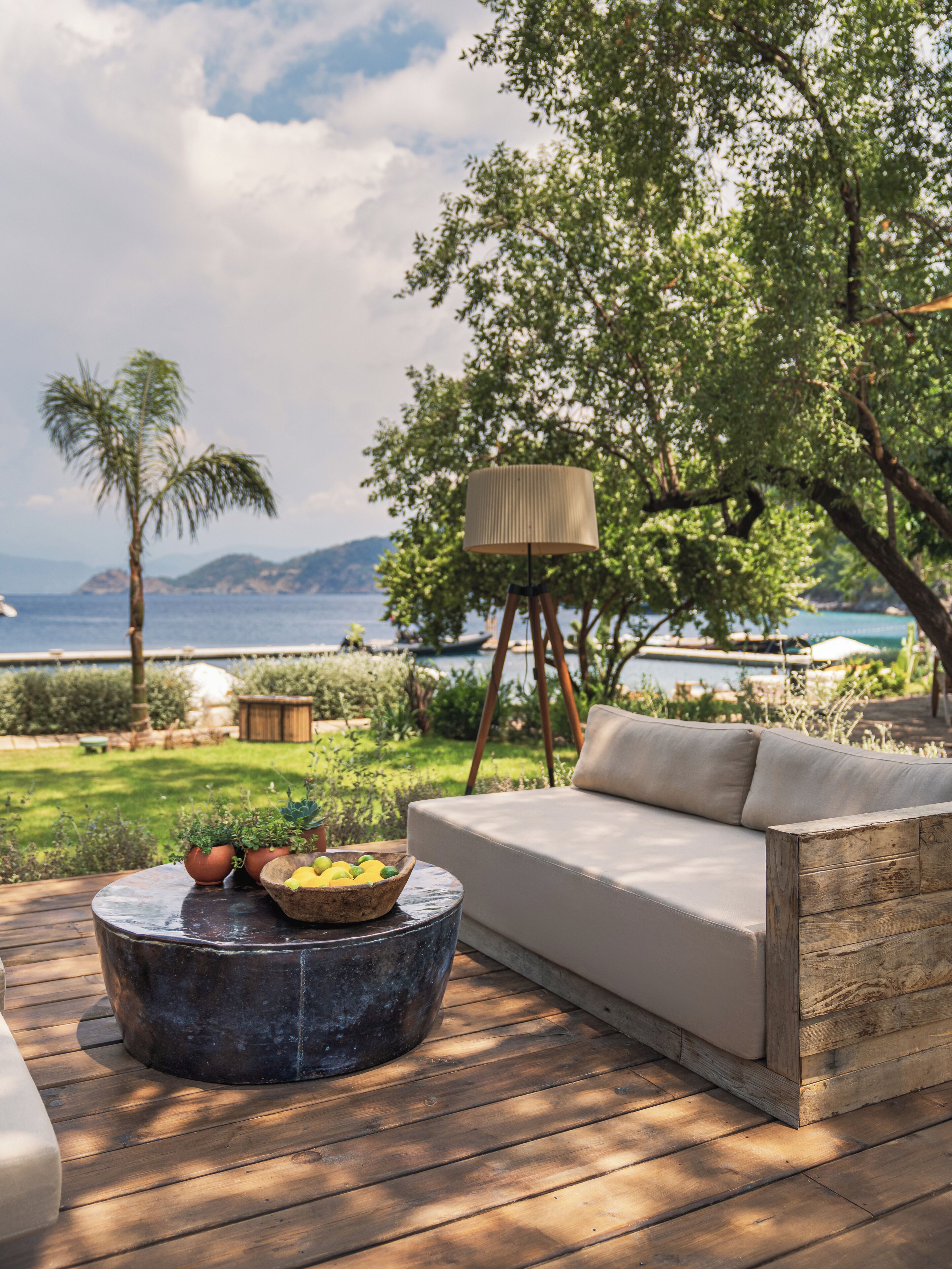 A wooden deck with a round table, a beige sofa, and a lamp.