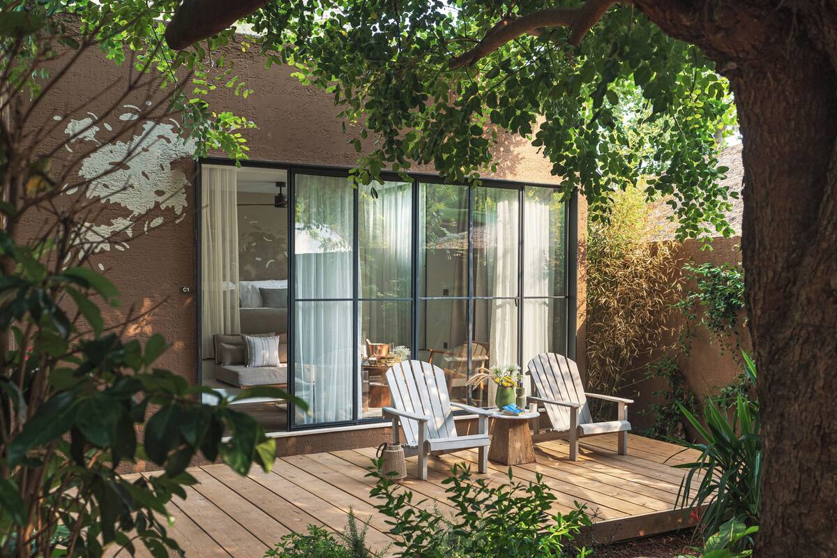 A modern outdoor seating area with a glass wall, wooden deck, and surrounding greenery.