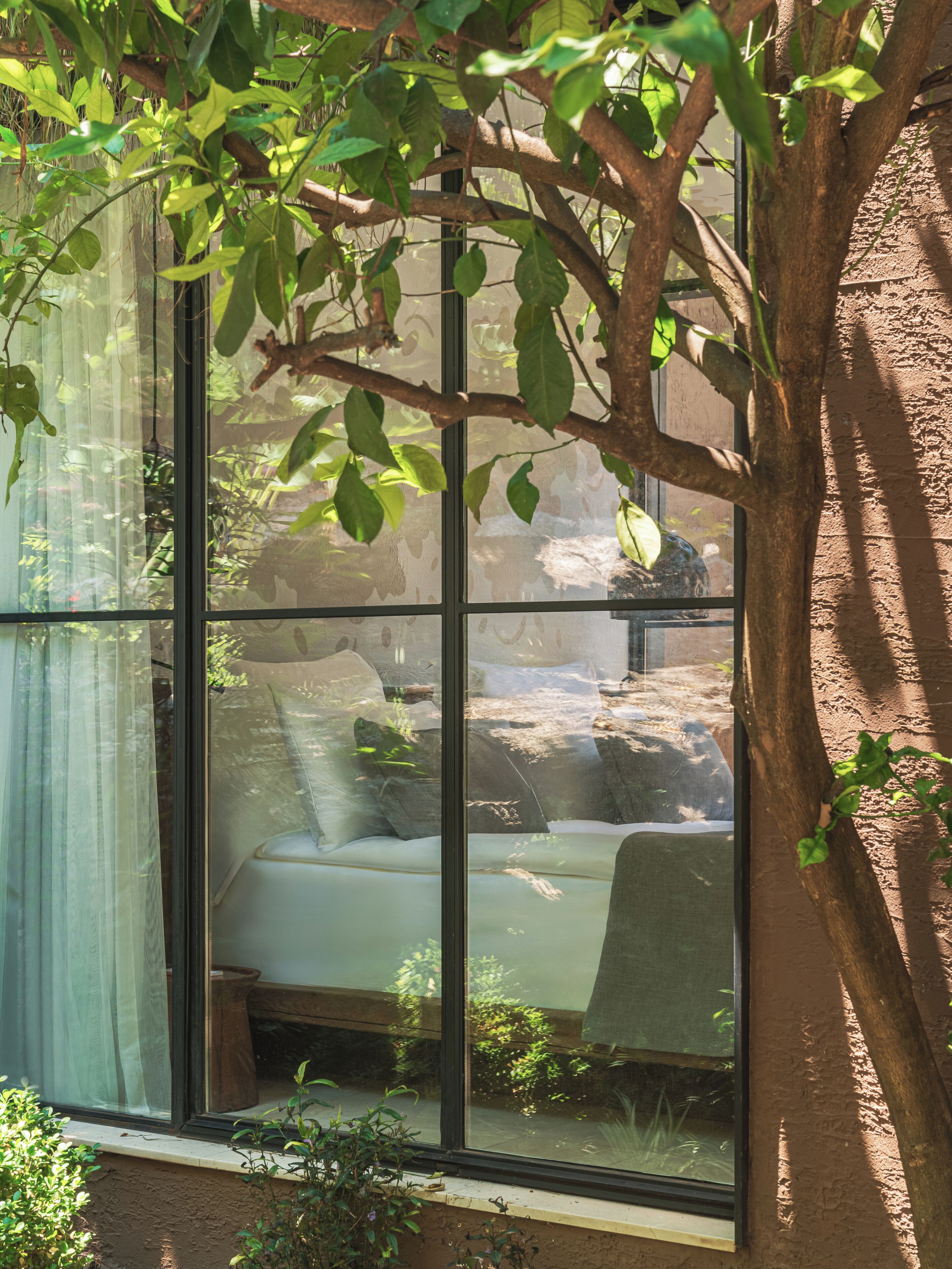 A room with a large window, a bed, and a view of a rocky outdoor area.