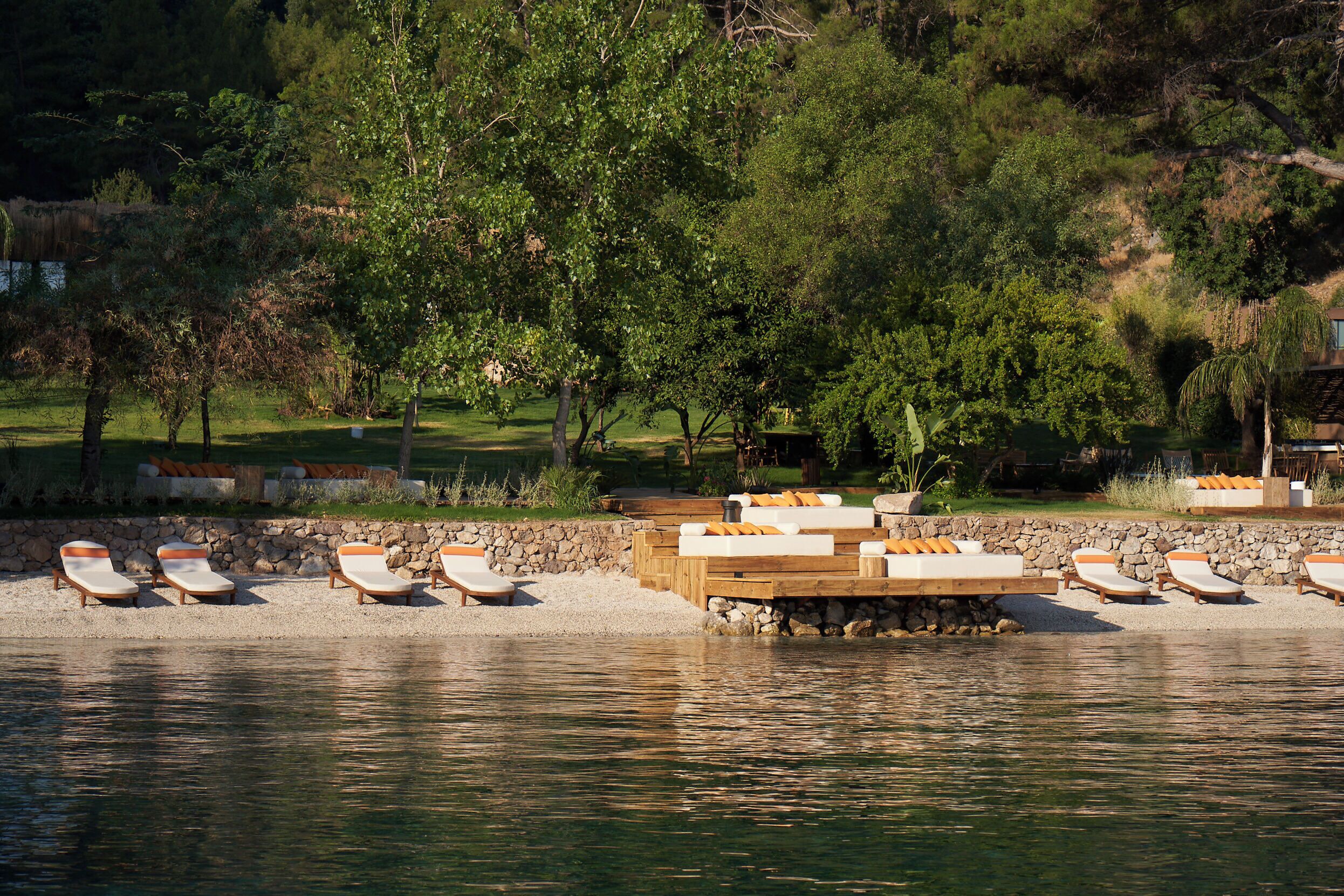 A lakeside resort with sun loungers and a wooden deck by the water.