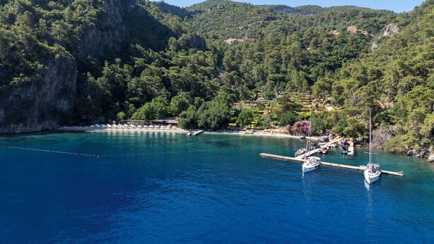 Une zone côtière où des bateaux sont amarrés à un quai, entourée de collines verdoyantes et d’une eau d’un bleu limpide.