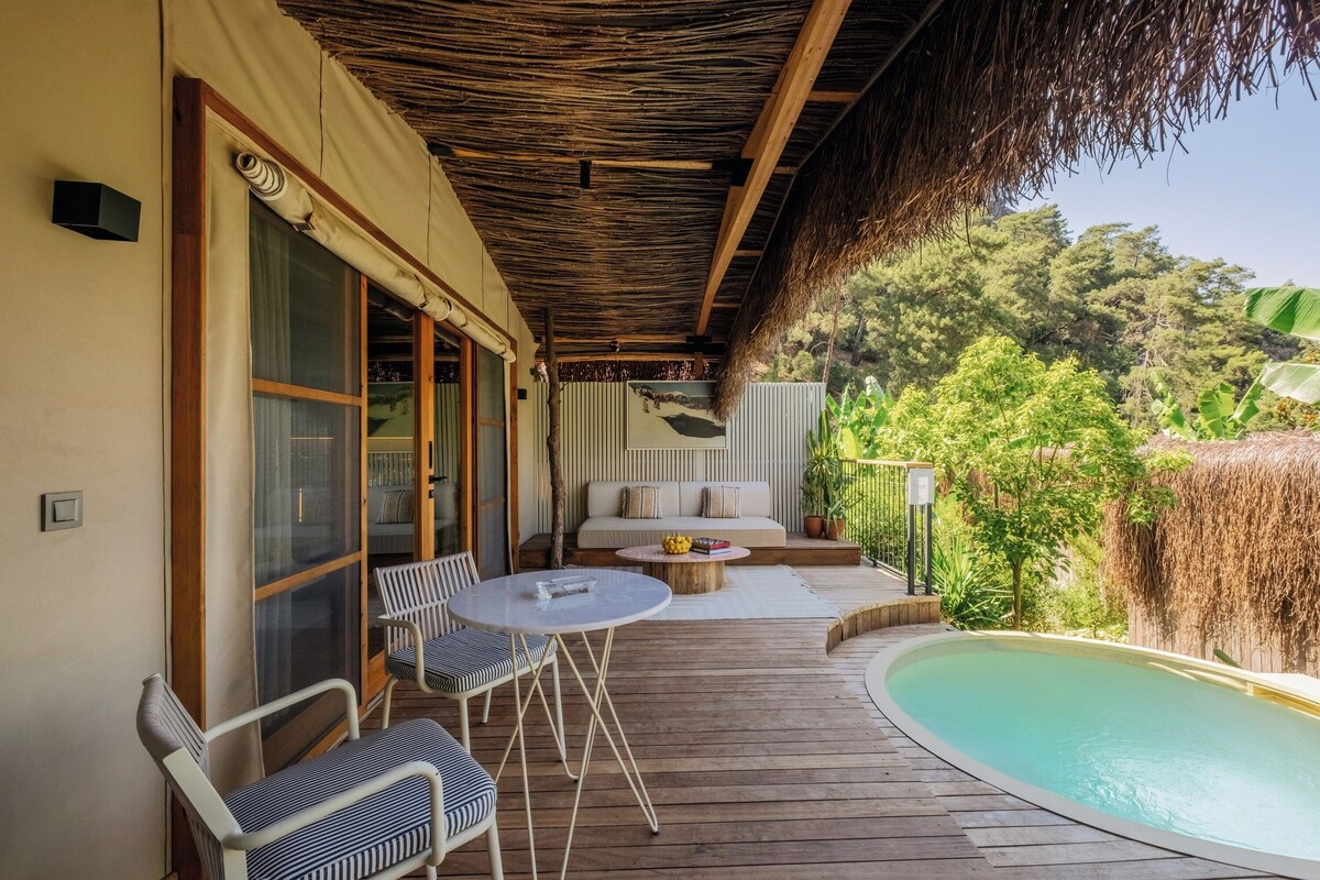 Eine Holzterrasse mit Pool, Sitzgelegenheiten im Freien und Blick auf die umliegende Grünfläche.