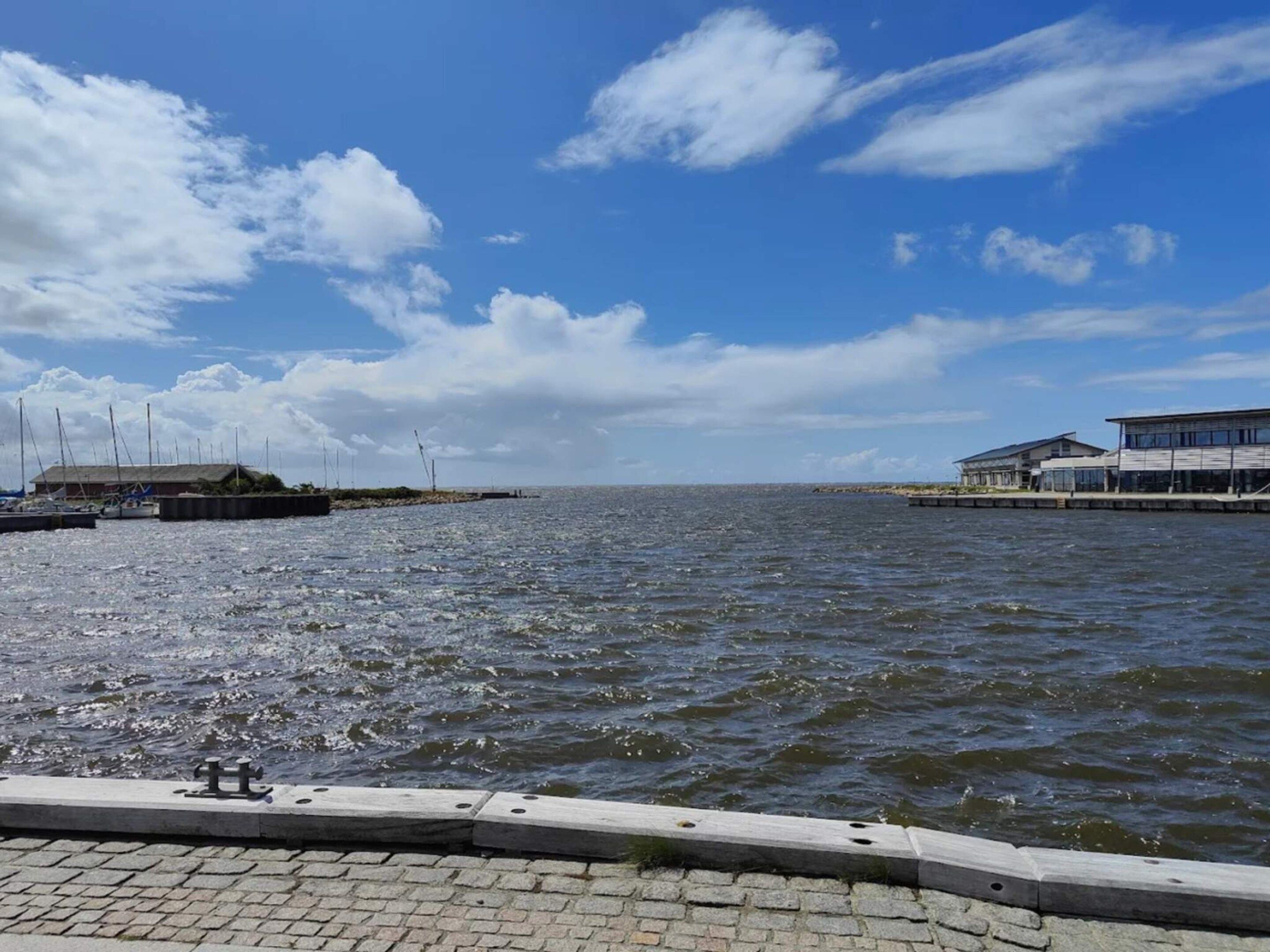 A waterfront view with a paved walkway, boats, and buildings along the shore.
