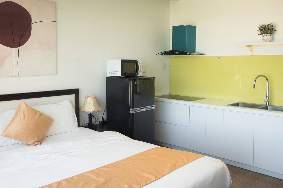 A hotel room with a bed, a black refrigerator, a microwave, a sink, and a small kitchen area.