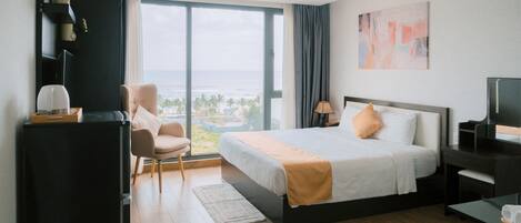 Habitación de hotel con una cama grande, un escritorio con lámpara, una silla y vista al océano.