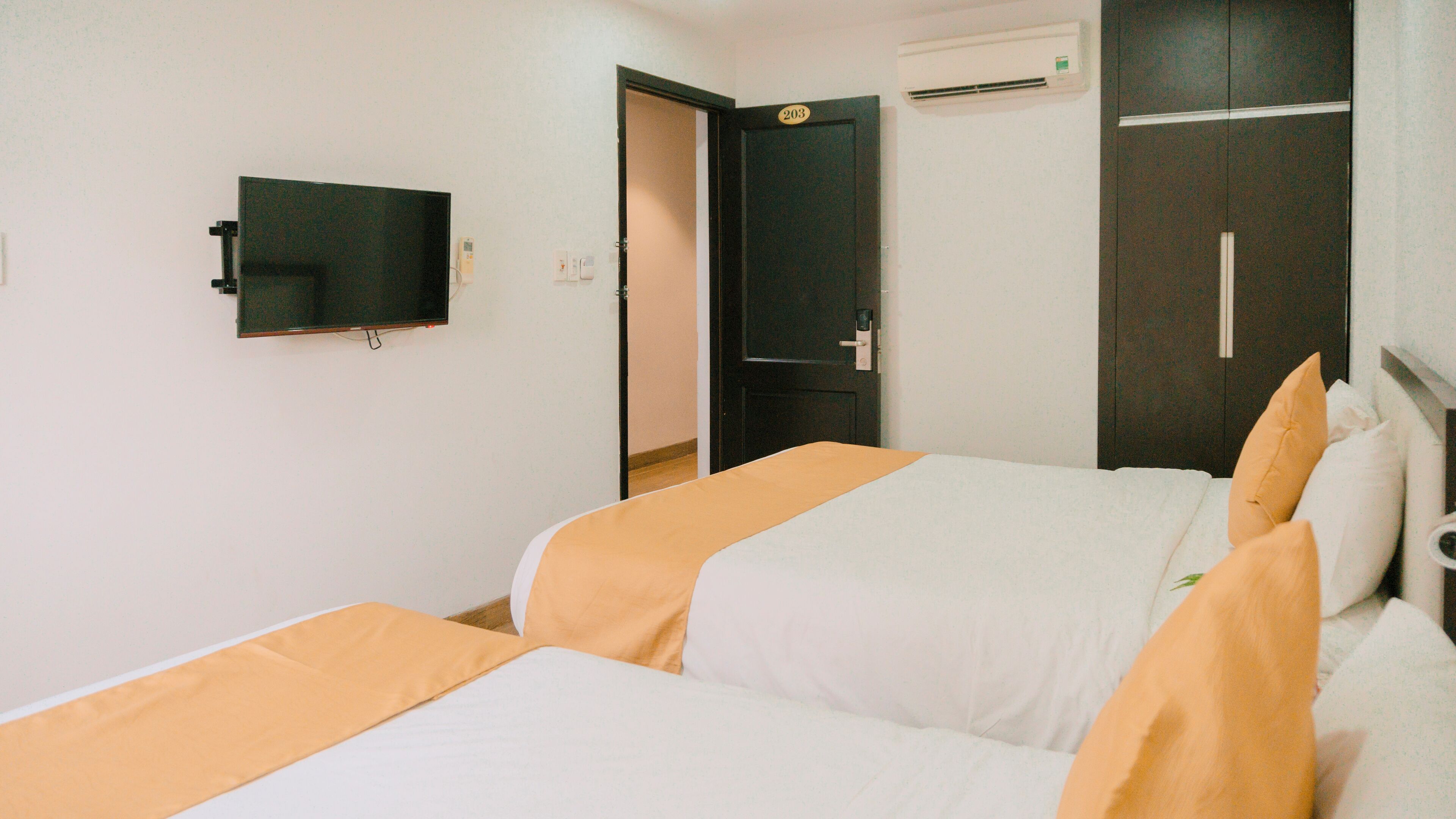 A hotel room with two beds, a TV, a wardrobe, and an air conditioning unit.