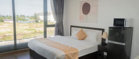 Habitación de hotel con una cama grande, una mesita de noche, un refrigerador y una ventana con vistas al exterior.