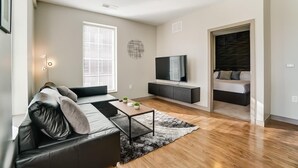 A modern living room with a sofa, coffee table, TV, and a view of a bedroom.