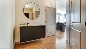 A hallway with a dark console, a round mirror, and a welcome sign.