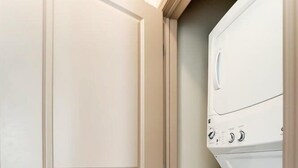 A laundry room with a door, a stacked washer and dryer, and a wooden floor.