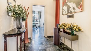 A hallway with a dark wooden console table, a tall vase with green plants, a tall vase with yellow flowers, and a large abstract painting on the wall. - Trastevere 319 in Rome (Rome)