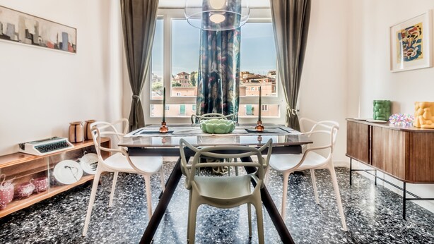 A modern dining area with a table and chairs, a decorative hanging light, and a view of buildings through large windows. - Trastevere 319 in Rome (Rome)