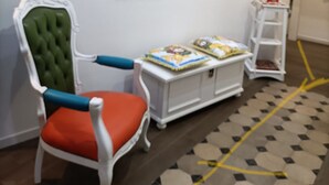 A room with a map on the wall, a chair with a cushion, a small table with books, and a white shelf with decorative items. - Ortigia Sweet Home in Syracuse (Syracuse)