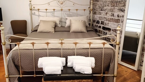 A neatly arranged bedroom with a metal bed frame, a wooden floor, a brick wall, and a mirror. - Ortigia Sweet Home in Syracuse (Syracuse)
