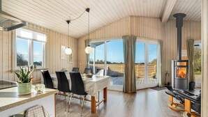 Ein geräumiges Zimmer mit Essbereich, Kamin und großen Fenstern mit Blick ins Freie.