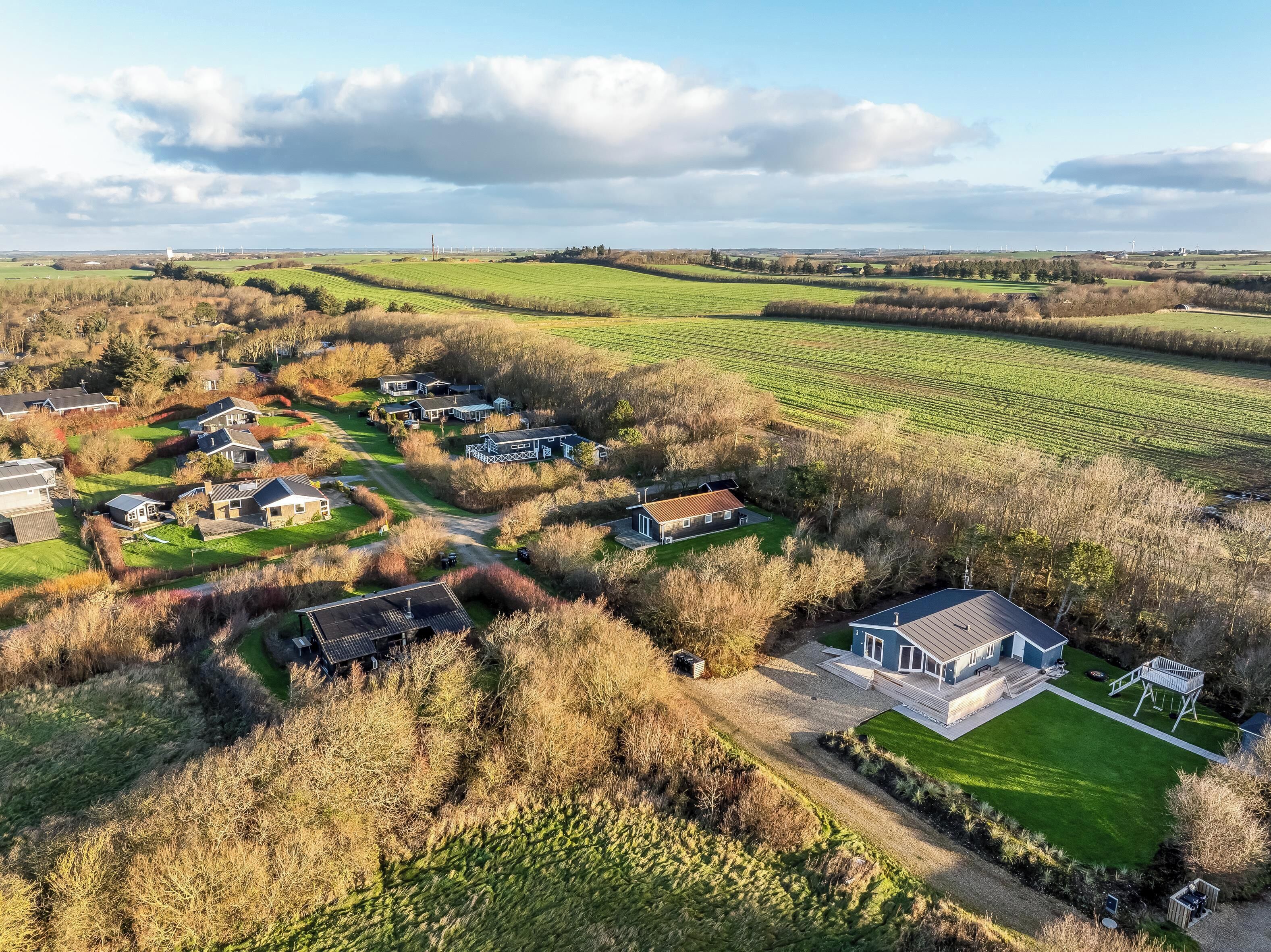 An aerial view of a residential area with houses, green fields, and a clear sky.