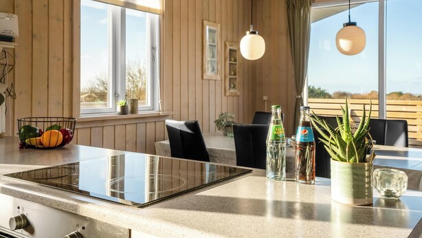 Eine moderne Küche mit Glaskochfeld, Holzwänden und einem Essbereich mit schwarzen Stühlen.