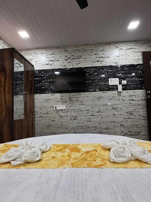 Quarto de hotel com cama, televisão fixada na parede e guarda-roupa de madeira.