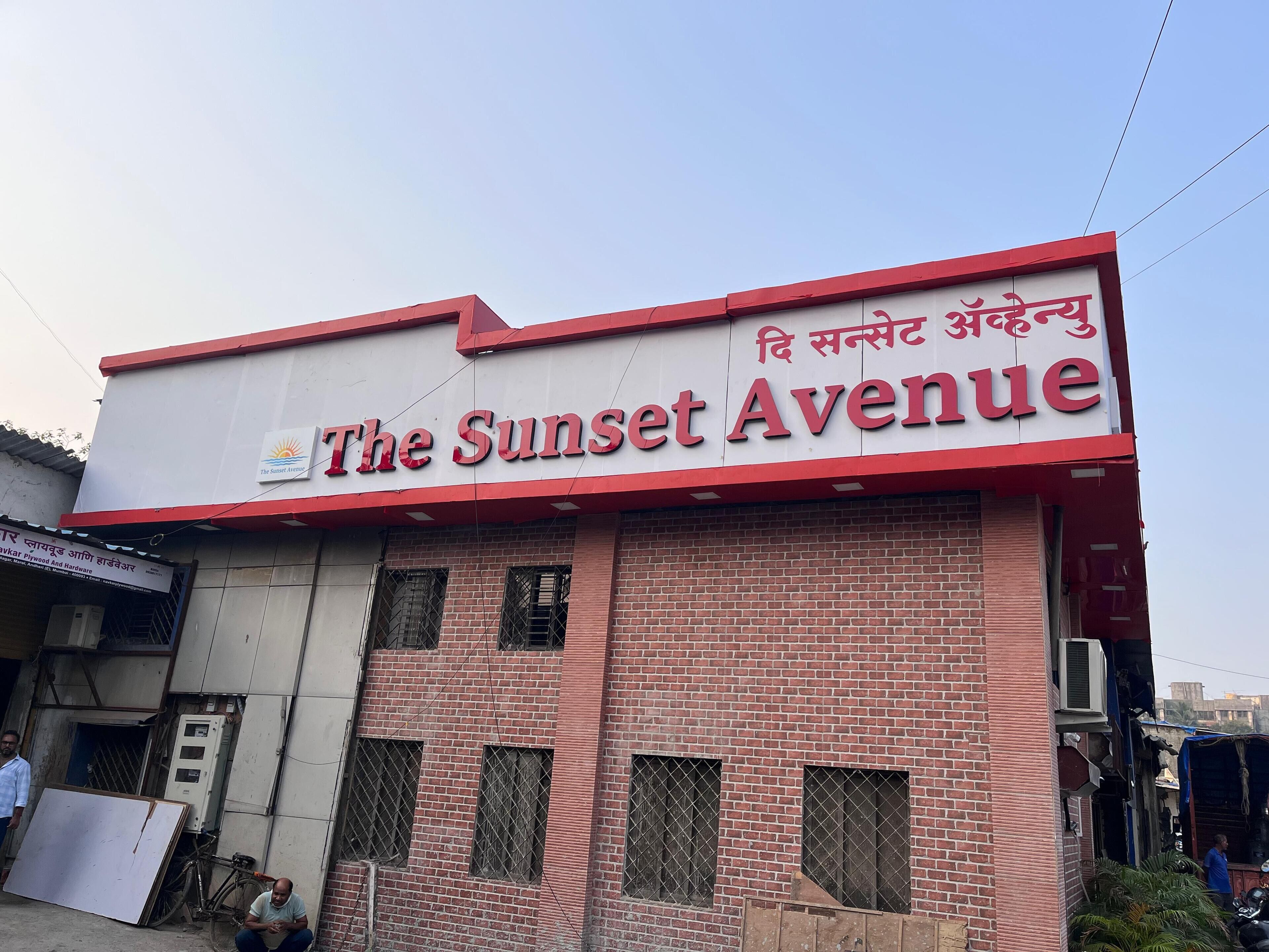 A building with a sign reading "The Sunset Avenue" in English and another language.