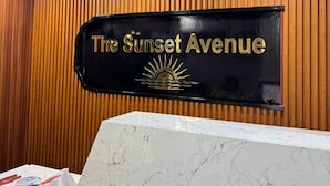 A reception desk with a sign that reads "The Sunset Avenue" and a logo of a sun above the text. - Hotel The Sunset Avenue (Mumbai)
